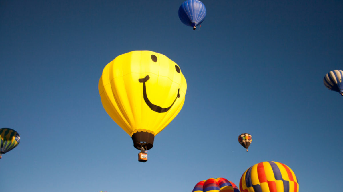 smiley face hot air balloon rising in the sky with other colorful balloons
