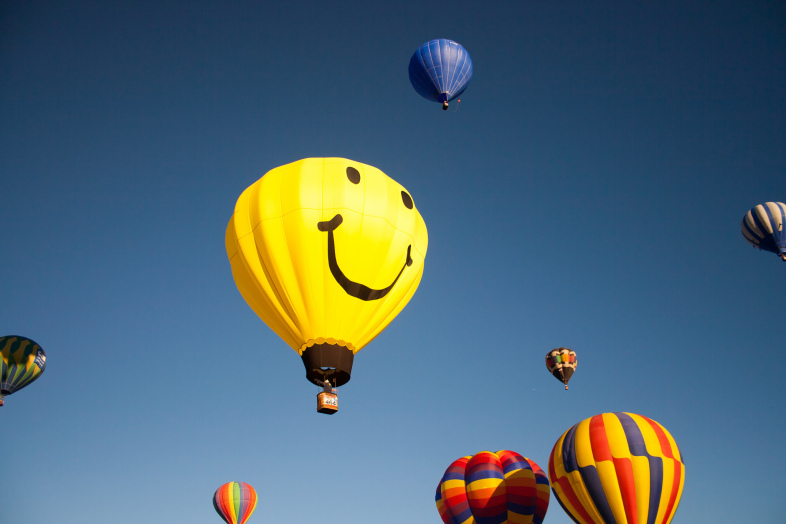 smiley face hot air balloon rising in the sky with other colorful balloons